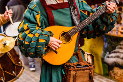 Midsection of man wearing traditional clothing while playing string instrument on road during parade