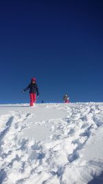 People skiing on snowcapped mountain against clear blue sky