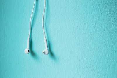 Close-up of in-ear headphones against blue wall