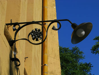 Low angle view of lamp mounted on wall against clear blue sky