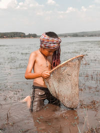 Midsection of shirtless man holding fishing net on beach