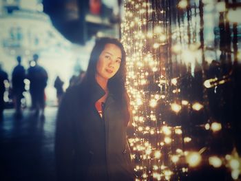 Portrait of smiling woman standing by illuminated decoration at night