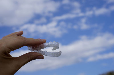 Cropped hand of person holding dentures against sky