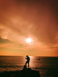 Silhouette person standing on sea against sky during sunset