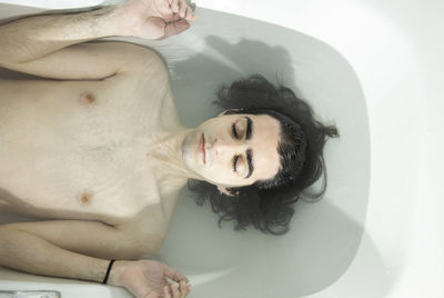 Shirtless man with eyes closed lying in bathtub