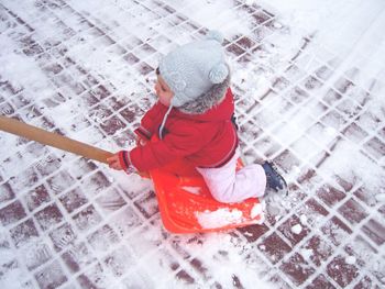 High angle view of child on shovel at snow covered footpath