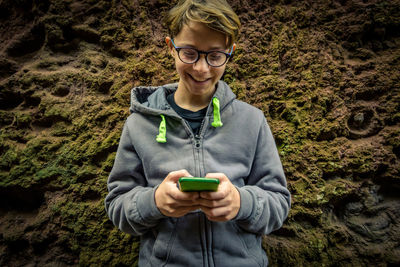 Close-up of smiling boy using smart phone standing by rock