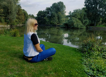 Side view of woman sitting on grass by lake