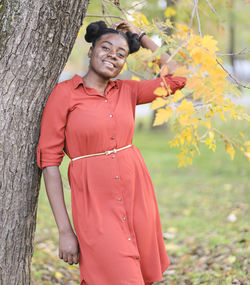 Portrait of smiling young woman standing by tree trunk