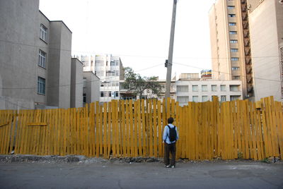 Full length rear view of man standing by wooden fence against buildings