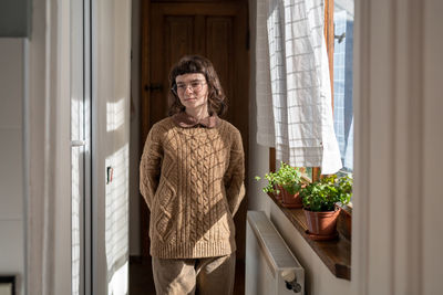 Portrait of young woman standing against window