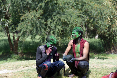 Men covered in powder paint while crouching on field against trees