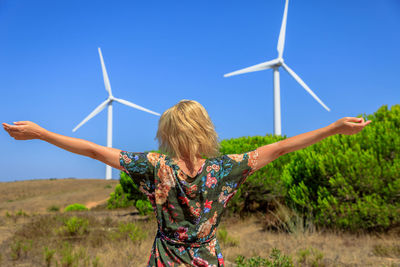 Rear view of woman with arms outstretched standing on land against sky