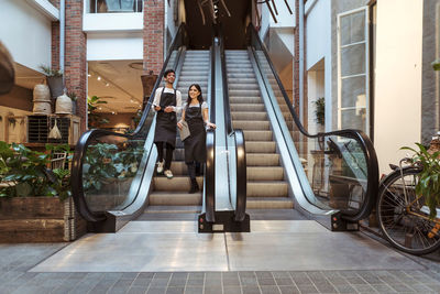 Smiling male and female coworkers standing on escalator in boutique