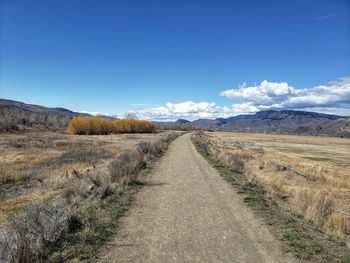 Road leading towards mountains against blue sky