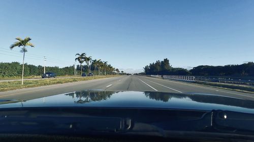 Road against clear blue sky seen through car windshield