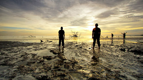 Silhouette people on beach against sky during sunset