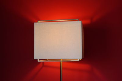 Close-up of illuminated modern lamp against red background