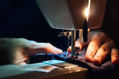 Cropped hands using sewing machine in darkroom