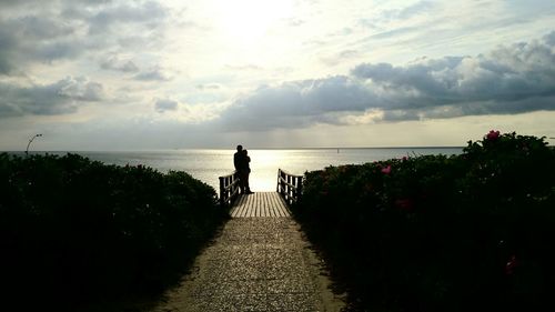 Silhouette man standing by sea against sky