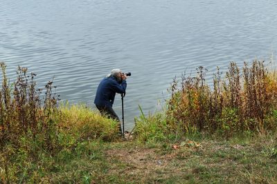 Full length side view of man photographing at lakeshore