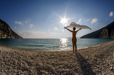 Woman standing at beach against sky during sunset