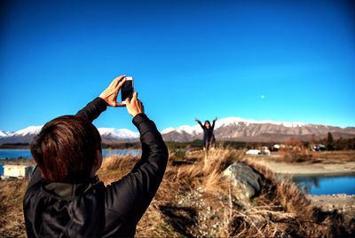 Woman photographing against clear blue sky