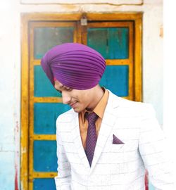 Smiling man in turban and suit standing against door