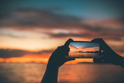 Person photographing orange sunset sky