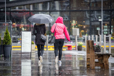 Rear view of women walking on footpath in rain