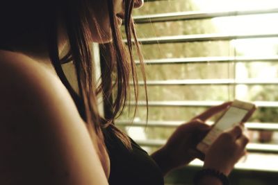 Midsection of woman using phone by window