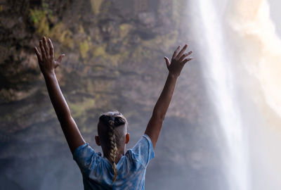 Teenage boy hands up and looking at the waterfall cascades before him.