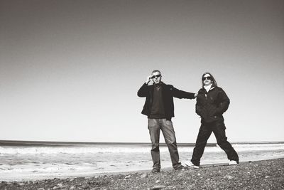 Full length of friends standing on beach against clear sky