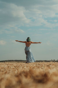 Rear view of woman with arms outstretched standing at beach