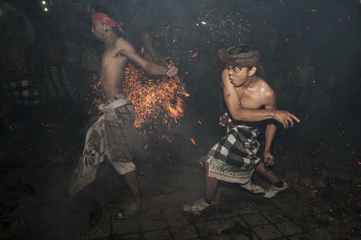 Shirtless men performing stunt with fire at night