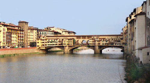 Arch bridge over river by buildings against clear sky