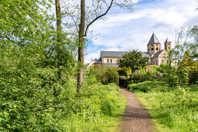 Footpath amidst trees and buildings against sky