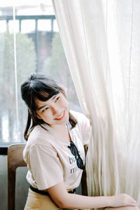 Young woman looking away while sitting on window