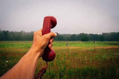 Close-up of hand holding red ball on field against sky