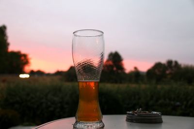 Close-up of beer glass on table against sky during sunset