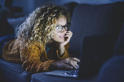 Smiling woman using laptop lying on sofa