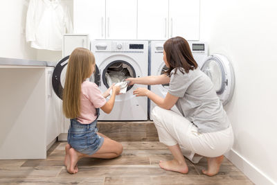 Mother and daughter pulling out clothes from washing machine at home