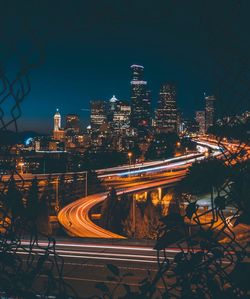 Illuminated light trails on road amidst buildings in city at night