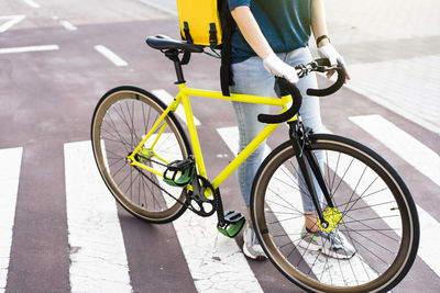 Young delivery woman with bicycle standing on zebra crossing