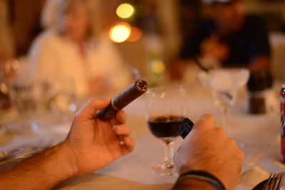 Cropped hand holding cigar by wineglass on table