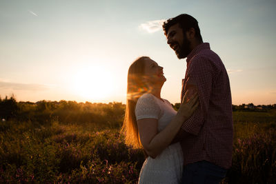Side view of couple kissing on field against sunset sky