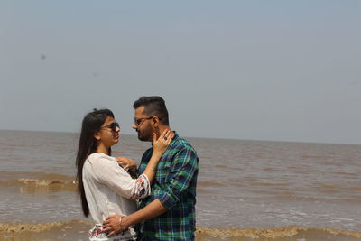 Young couple standing at beach against clear sky