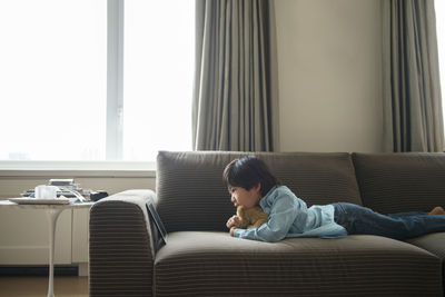 Boy looking at tablet while lying with stuffed toy on sofa at home