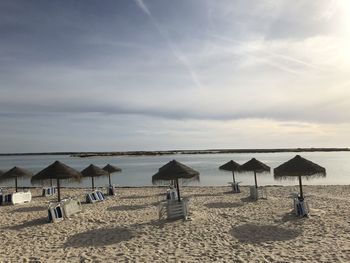 Lounge chairs and parasols on beach against sky