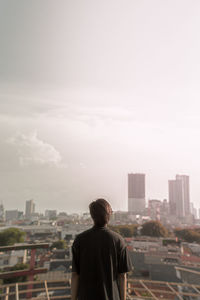 Rear view of man looking at cityscape against sky